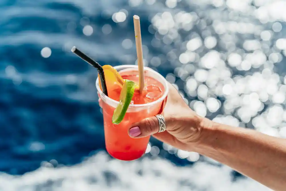 a cocktail held up against the sunlit sea