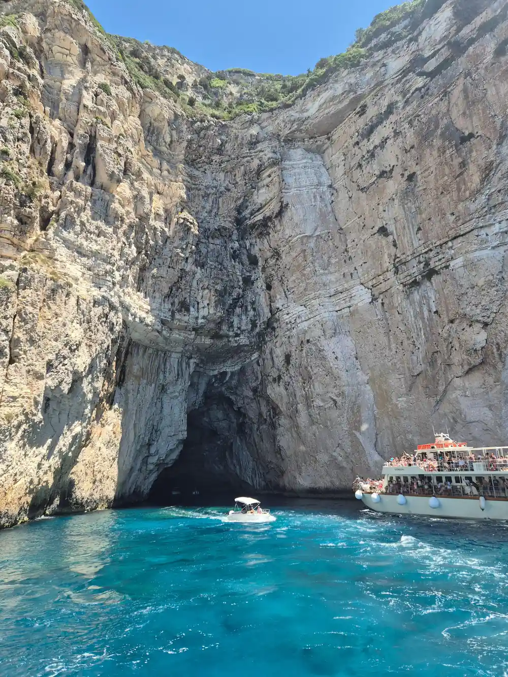 the cruise boat tiny against an enormous cave-riddled cliff