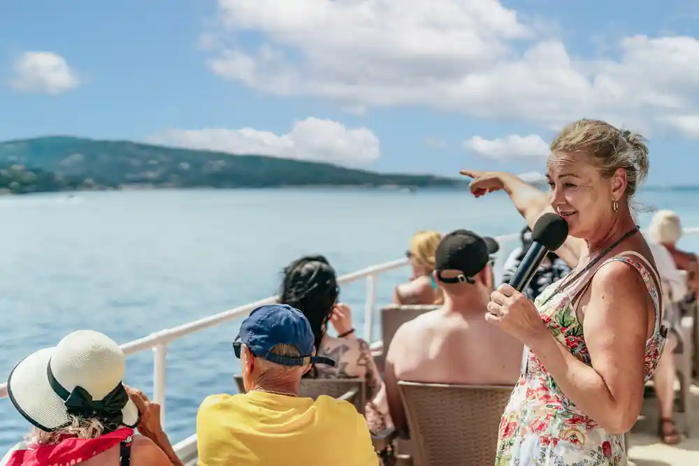 the guide with a microphone pointing something out to seated passengers