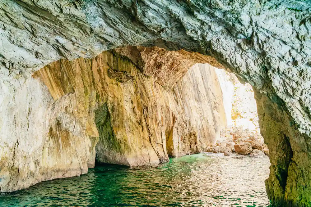 the inside of a sea cave with golden rock above deep green water