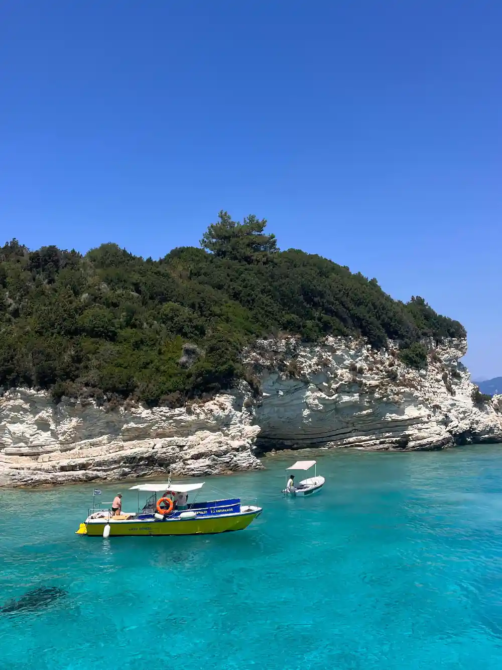 a launch crossing turquoise water below a wooded rocky point