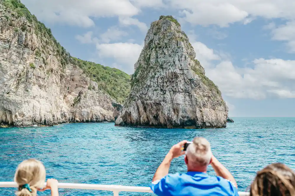 a passenger photographing a tall pointed sea stack from the rail