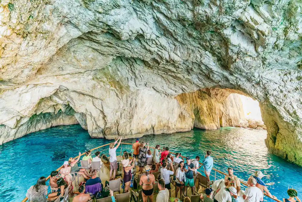 passengers on the bow cheering as the boat noses into a pale limestone cave mouth