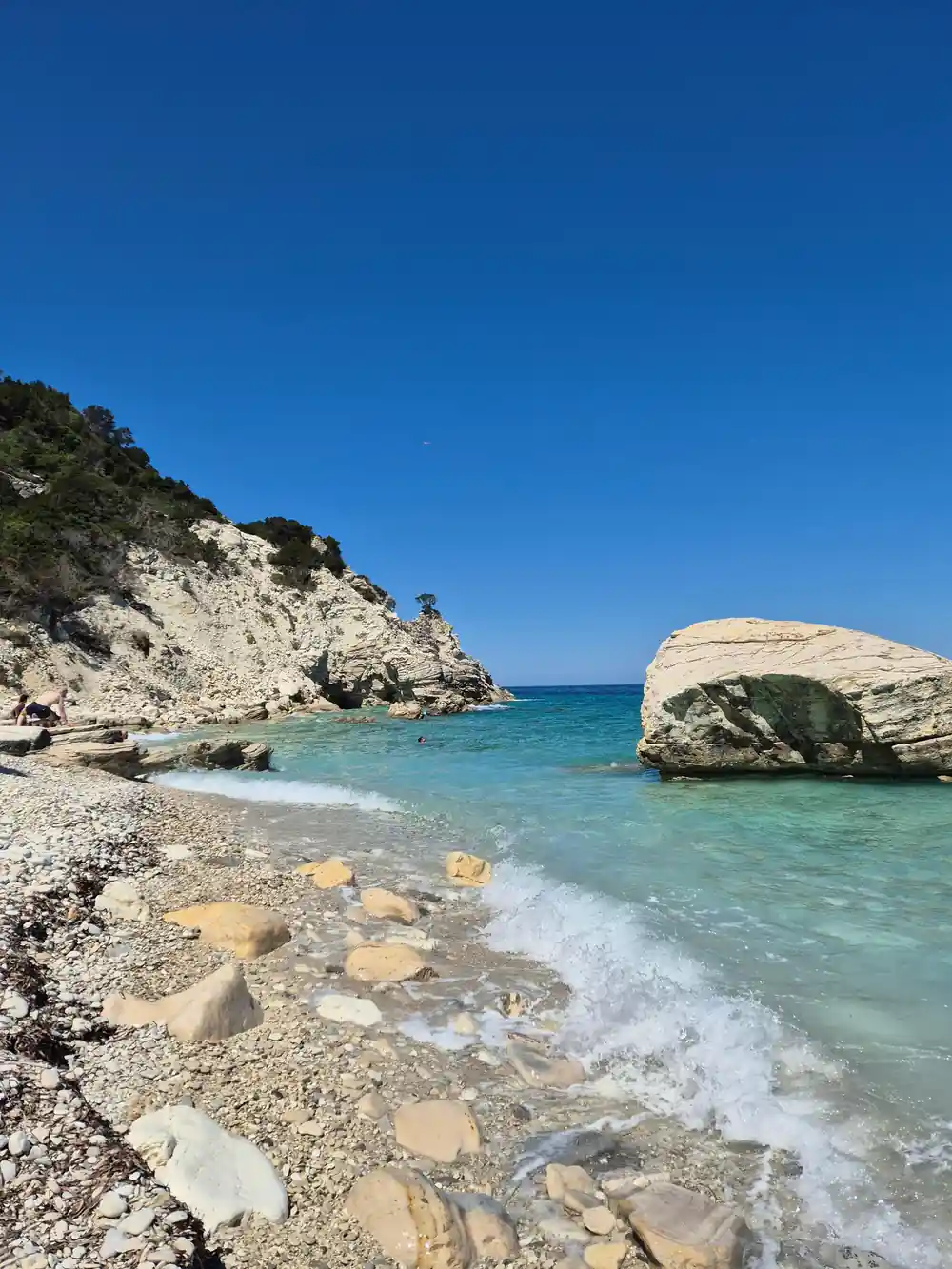 a pebble cove with white boulders and clear water at the edge