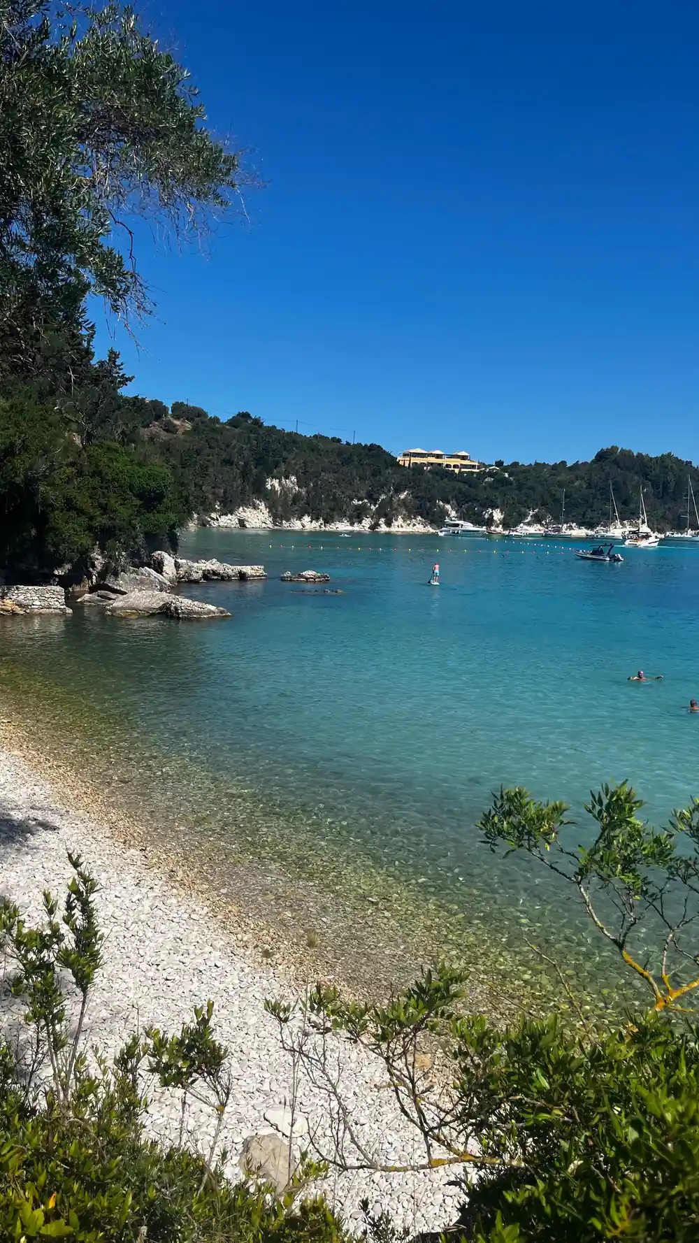 a quiet cove with a few swimmers and buildings up the hillside