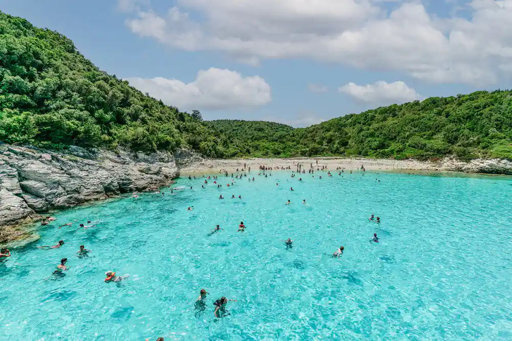 swimmers spread across brilliant turquoise shallows below a green headland