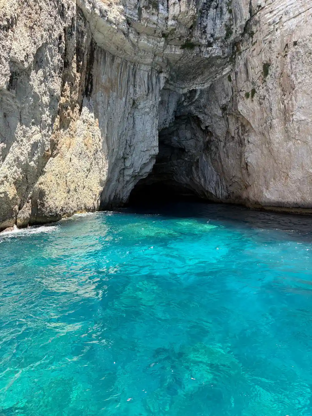 a wide cave entrance with brilliant turquoise water at its mouth