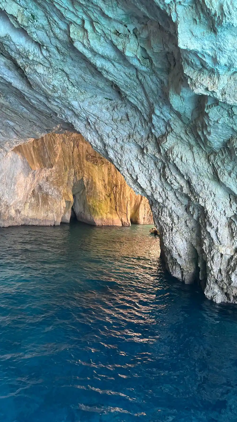 a wide cave entrance with orange and white rock above green water