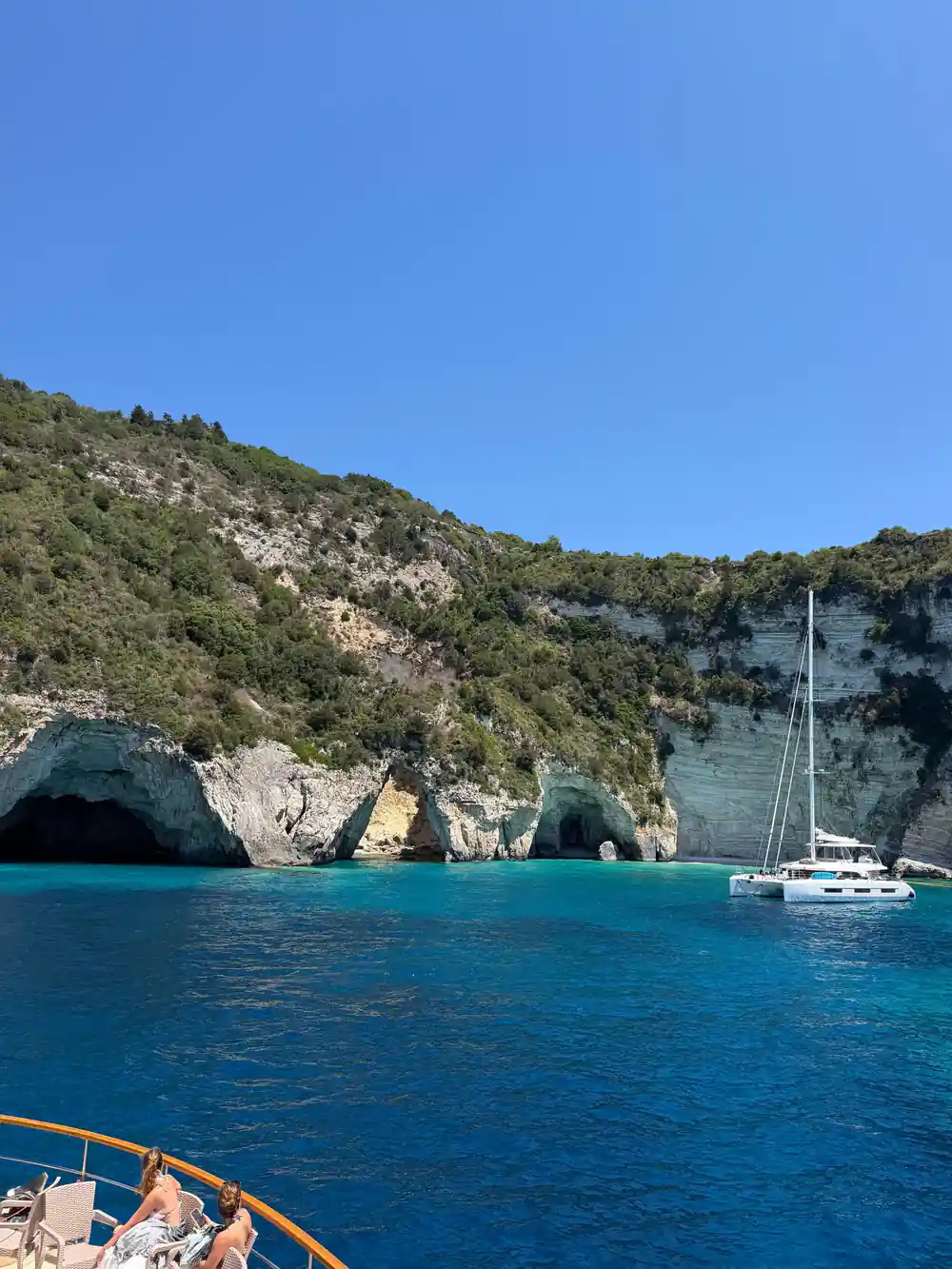 a yacht at anchor below a wooded headland with caves at the waterline