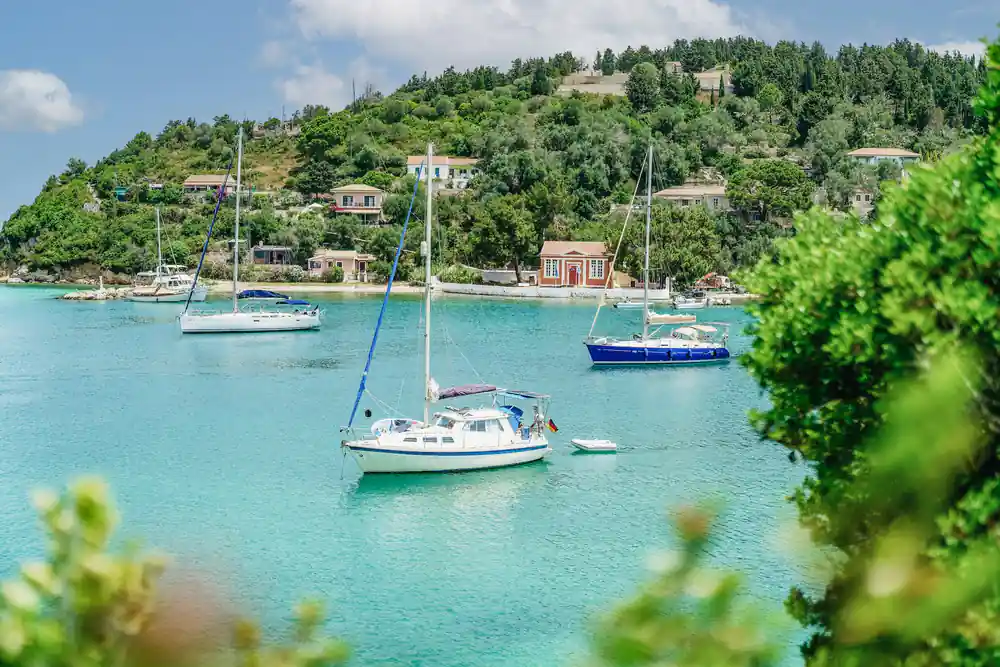 yachts moored in the sheltered natural bay at Lakka with village houses behind